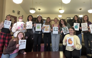 A group of student holding up coloring pages, smiling at the camera.